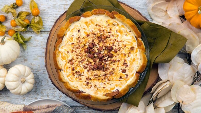 Overhead shot of an ice cream pie in a clear pie plate sitting on a wooden cutting board. It's on a grey wooden table with mini white pumpkins around it. 