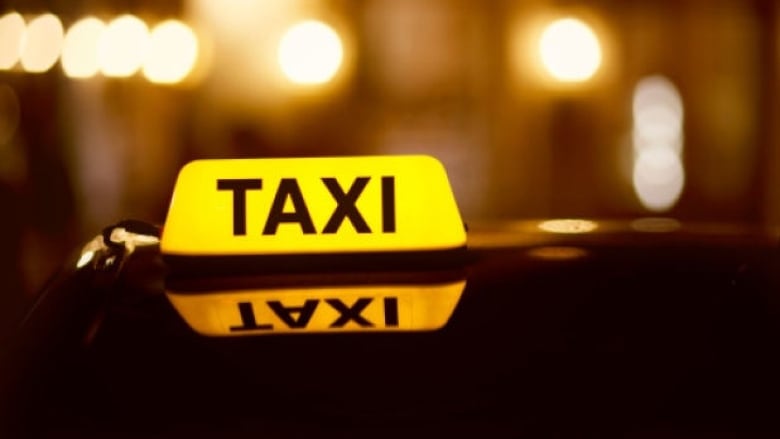 A stock image of a taxi at night shows the top of a car and a yelllow rooflight reading TAXI