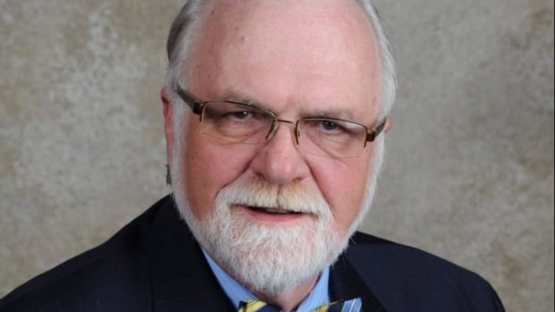 man with black glasses and white hair wearing a suit. 