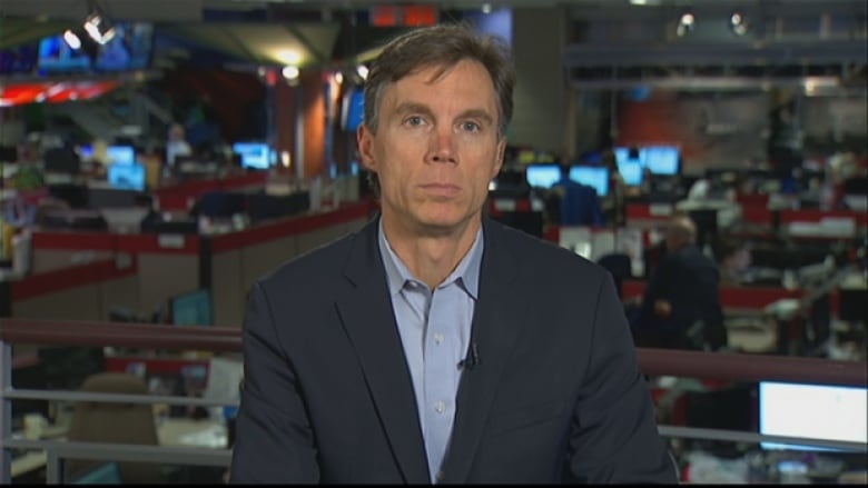 Man with brown and grey hair stands in a newsroom.