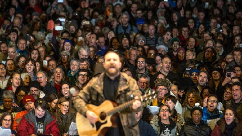 A concert crowd sings in unison behind a guitar player on stage.