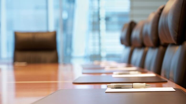 Notepads and pens are placed on a boardroom table surrounded by five empty seats.