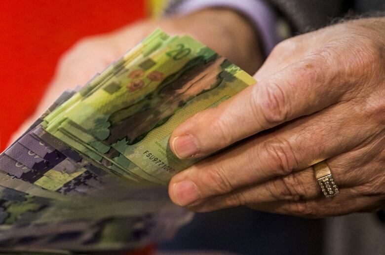 Two hands can be seen sifting through a series of dollar bills, mostly tens and twenties.