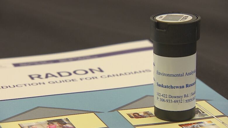 A small black container to collect radon sits on top of an information pamphlet