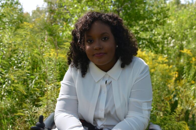 A woman sits in a wheelchair surrounded by trees. 