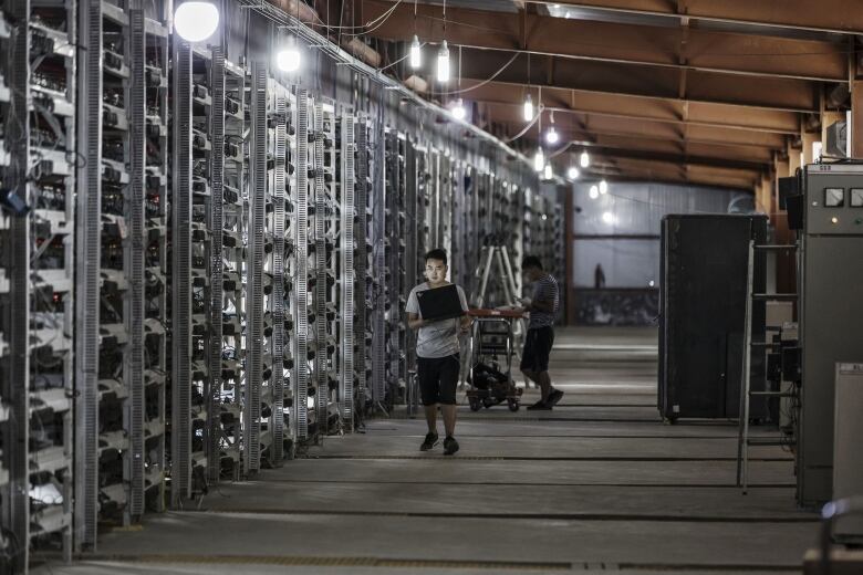 A person with a laptop walks beside a row of floor-to-ceiling computer servers.