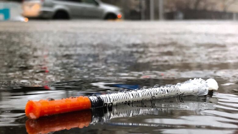 A hypodermic needle on the wet ground.