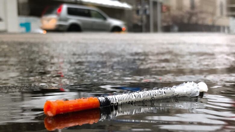 A hypodermic needle on the wet ground.