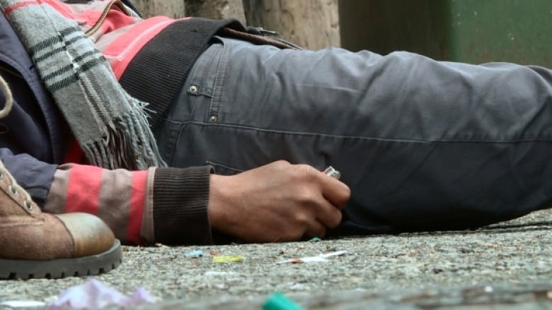 A person lays on their back while holding drug paraphernalia.