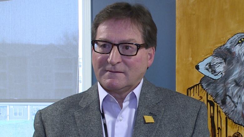 A man is wearing black rimmed glasses and a grey suit jacket. 