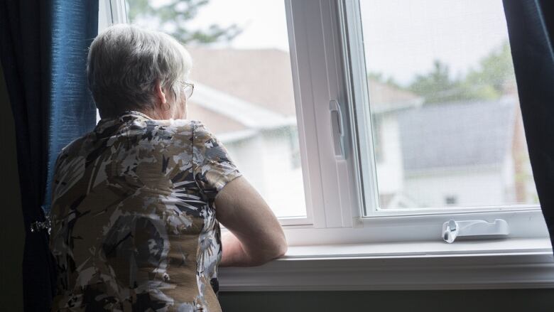 An older woman looks out of a window