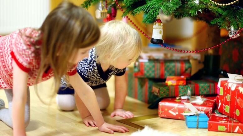 Children look at Christmas presents under a tree. Stock photo