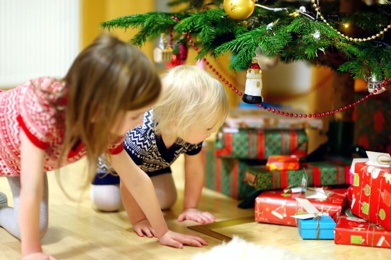 Children look at Christmas presents under a tree. Stock photo