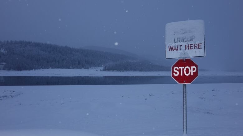 A stop sign in front of a partially-frozen river in the twilight.