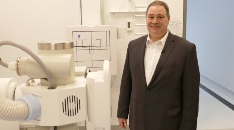 A man wearing a black suit stands in front of a diagnostic imaging machine. 