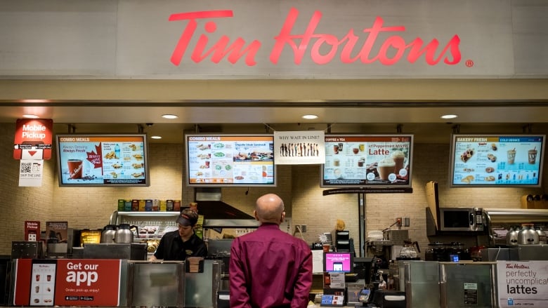 A customer at a Tim Hortons reads the menu while a worker makes a drink behind the counter.