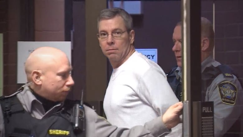 A handcuffed man is shown with two sherrif's deputies.