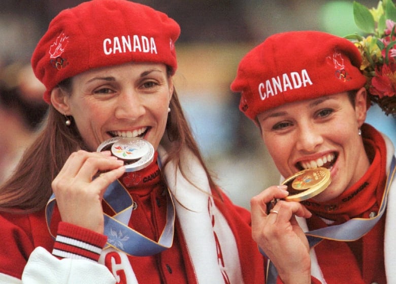 Two athletes in hats that say  Canada bite Olympic medals