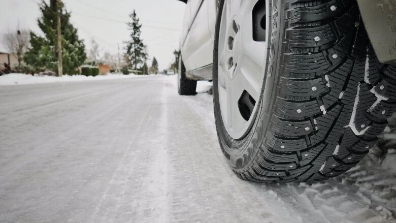 A close-up image of a snow tire on a vehicle driving on a snow-covered road.