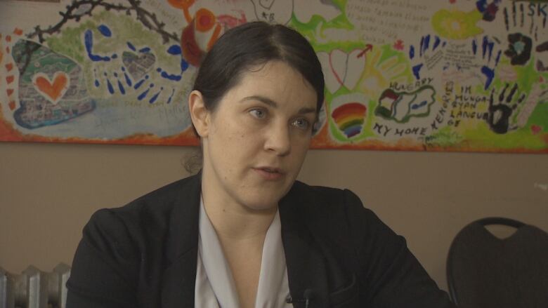 A woman in a black jacket faces right as she speaks to the camera.