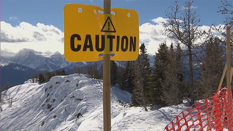 A caution sign sits next to the edge of a mountain.