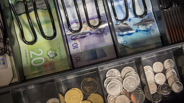 A closeup of a cash register drawer shows rows of bills and coins.