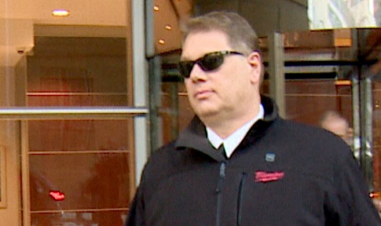 A man in sunglasses and a black coat walks out of the Calgary courthouse. 