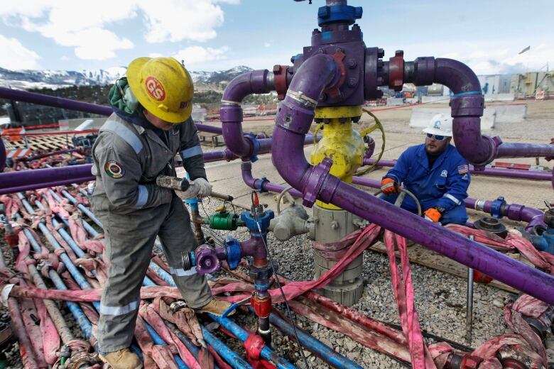 Two workers are seen among a series of pipes. They appear to be fixing some of them.