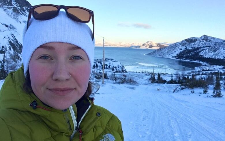 A woman smiles. There are mountains behind her covered in snow. 