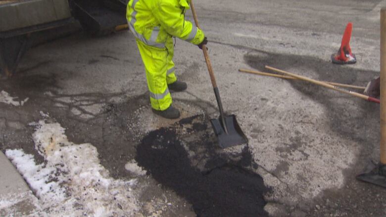 Person in a yellow neon work suit patches a pothole