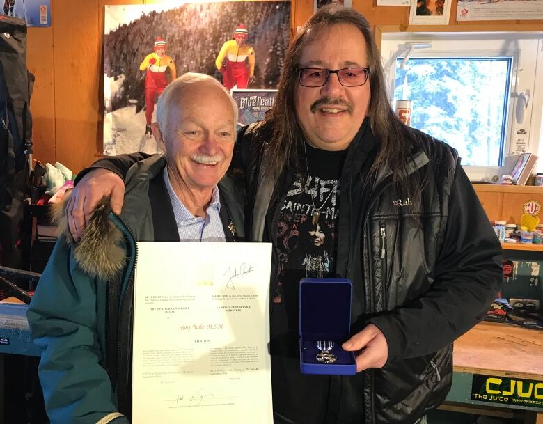 Two men pose holding a piece of paper and a medal.