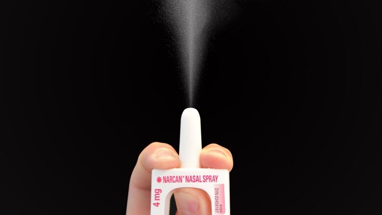 A person's left hand holding a dose of Narcan and dispensing the nasal spray into the air to demonstrate how it's used in a person's nose.