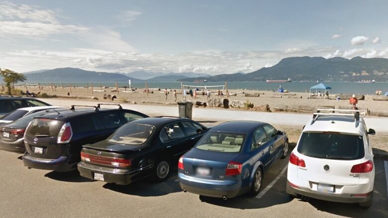 Vehicles are parked in a row in front of a sandy beach.