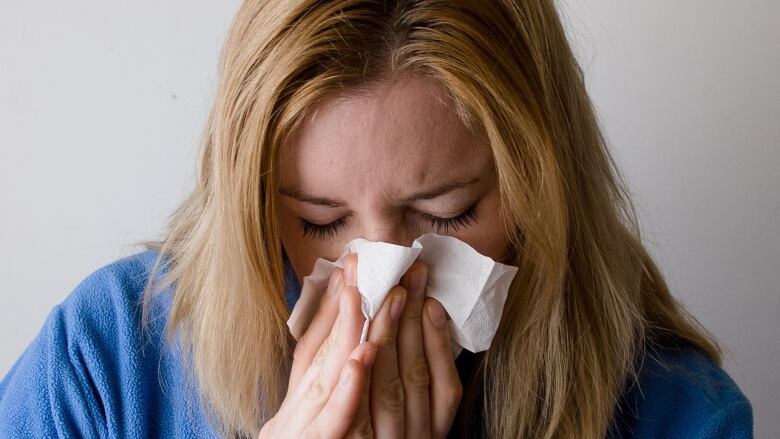 Woman sneezing and using a tissue.