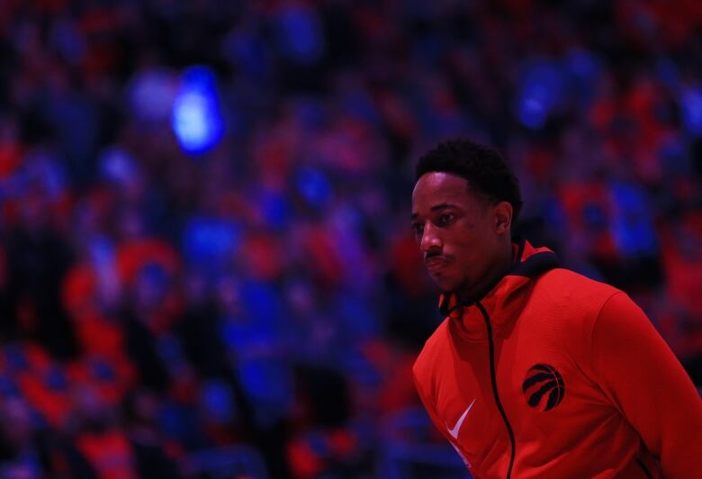 DeMar DeRozan stands on court with the lights off in the stadium, and fans watching.