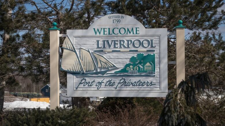 A white wooden sign nestled amongst trees says Welcome to Liverpool, Port of the Privateers. There is a carving of a sailboat in the sign