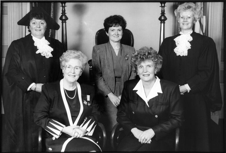 Five women pose, two of them in ceremonial gowns.