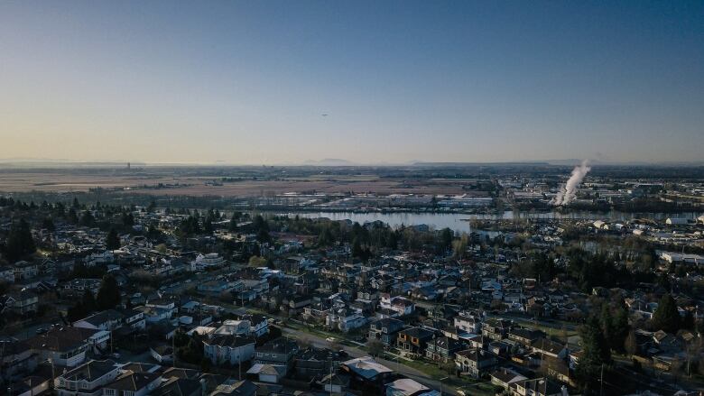 A smokestack is seen off in the background of this aerial shot of Fraserview and the Fraser River in South Vancouver. Rows of single-family homes are visible.