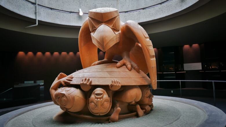 A wooden sculpture of a raven on top of three men.