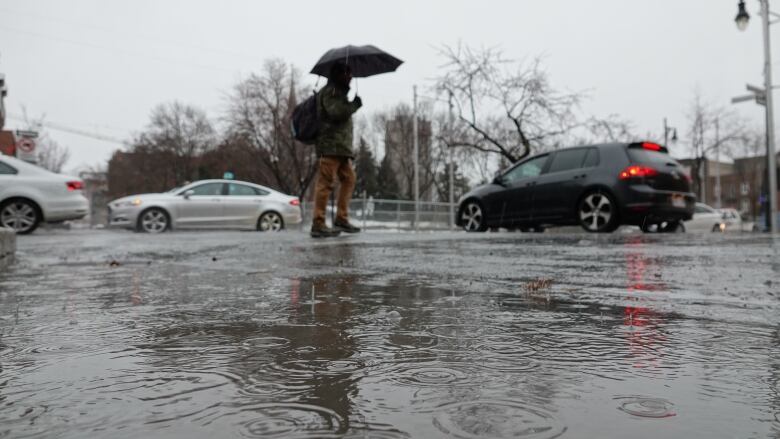 A person holding an umbrella as rain splashes into a puddle in the street. 