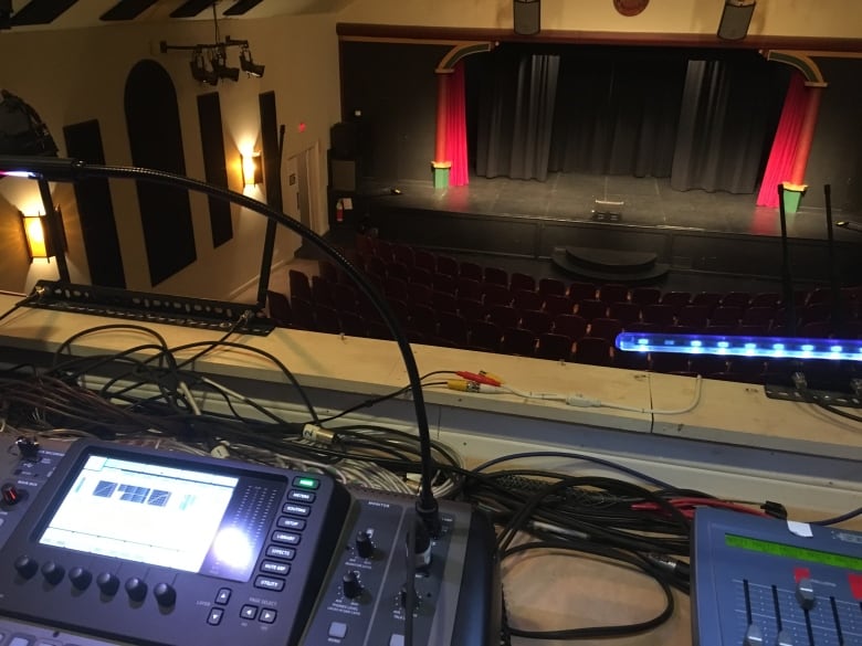 A sound board overlooks a theatre with a black stage.