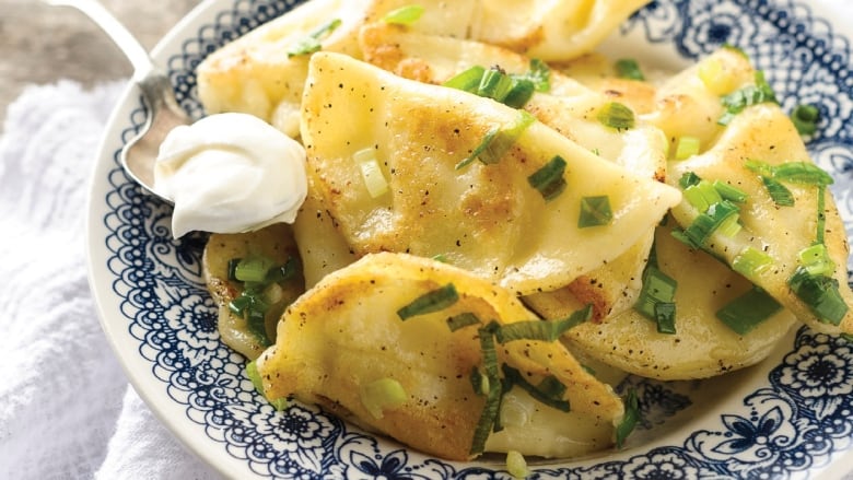 Closeup on a plate of perogies with a spoon with sour cream resting on the side.