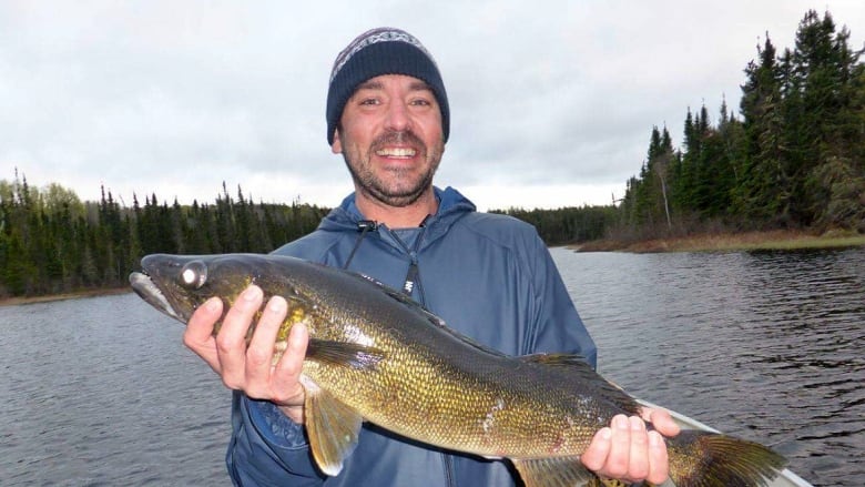 A smiling man in a boat holds up a fish.