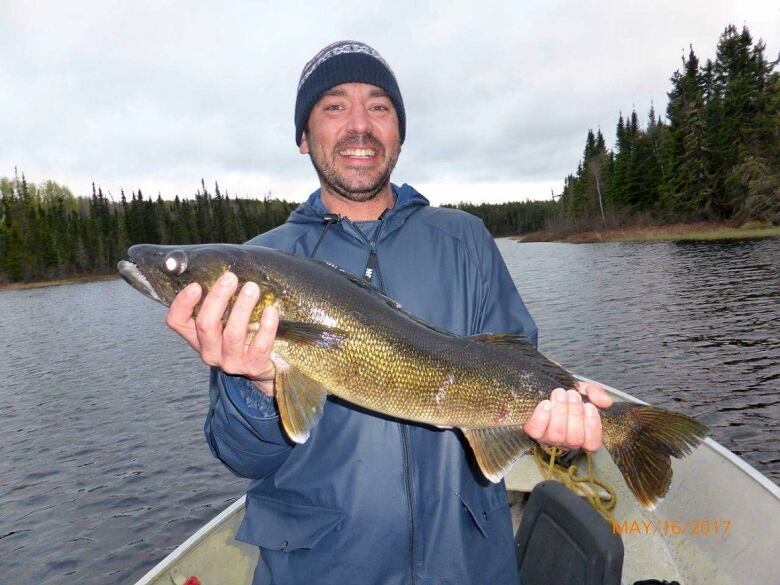 A smiling man in a boat holds up a fish.