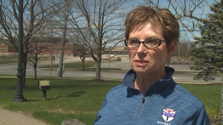 A woman standing outside wearing a blue quarter-zip sweater with a Rothesay logo on it.