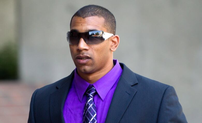 Josh Boden wears wraparound sunglasses, a navy blue suit and a purple shirt outside a Vancouver court.