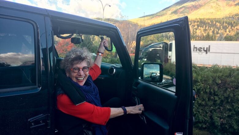 A smiling woman getting out of the passenger side of a jeep.