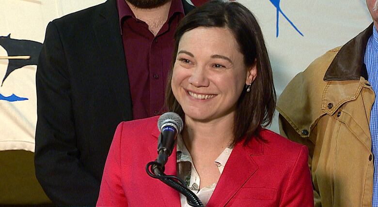 a woman in red jacket smiles at a microphone