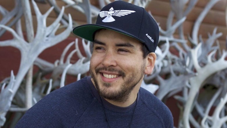 A man wearing a baseball cap smiles and looks to the side 