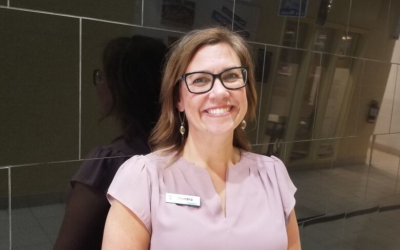 smiling woman with blonde hair, glasses, gold earrings and pink shirt